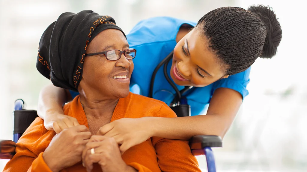A carer holding the hands of an older woman at home