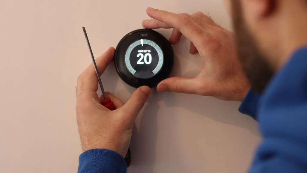 Is a Smart Thermostat Worth It? 6 Honest Checks Person fitting a smart thermostat to a wall, a job to consider when asking is a smart thermostat worth it