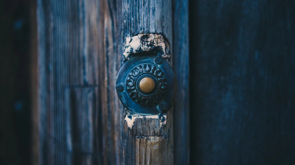Old round doorbell button on a weathered blue door