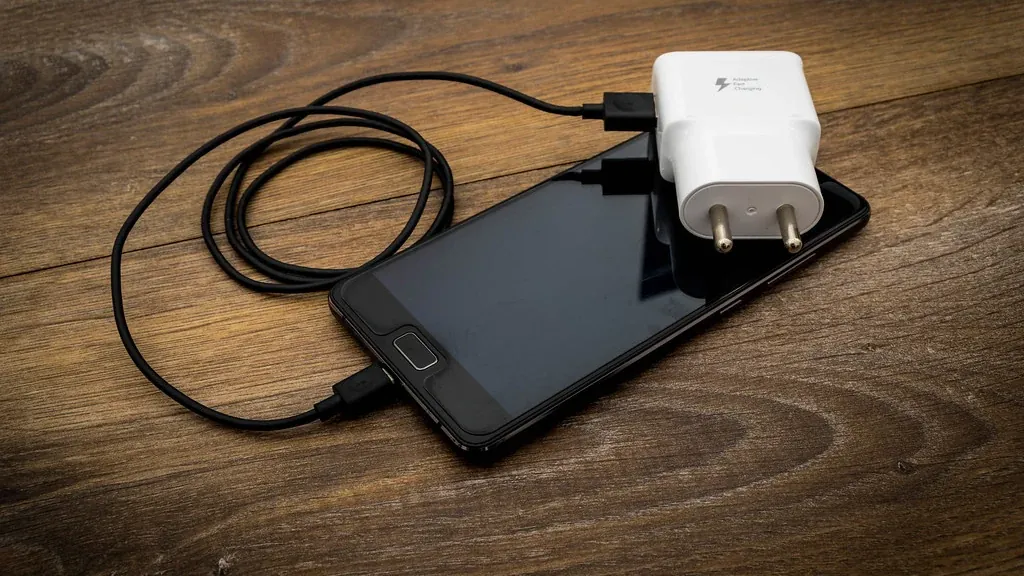 Phone charging on a wooden table, the kind of standby load a smart plug can switch off